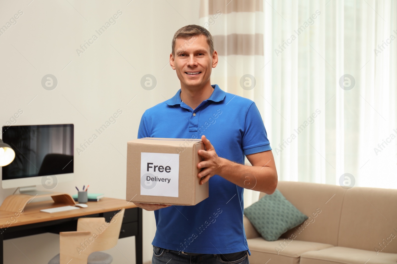 Photo of Courier holding parcel with sticker Free Delivery indoors