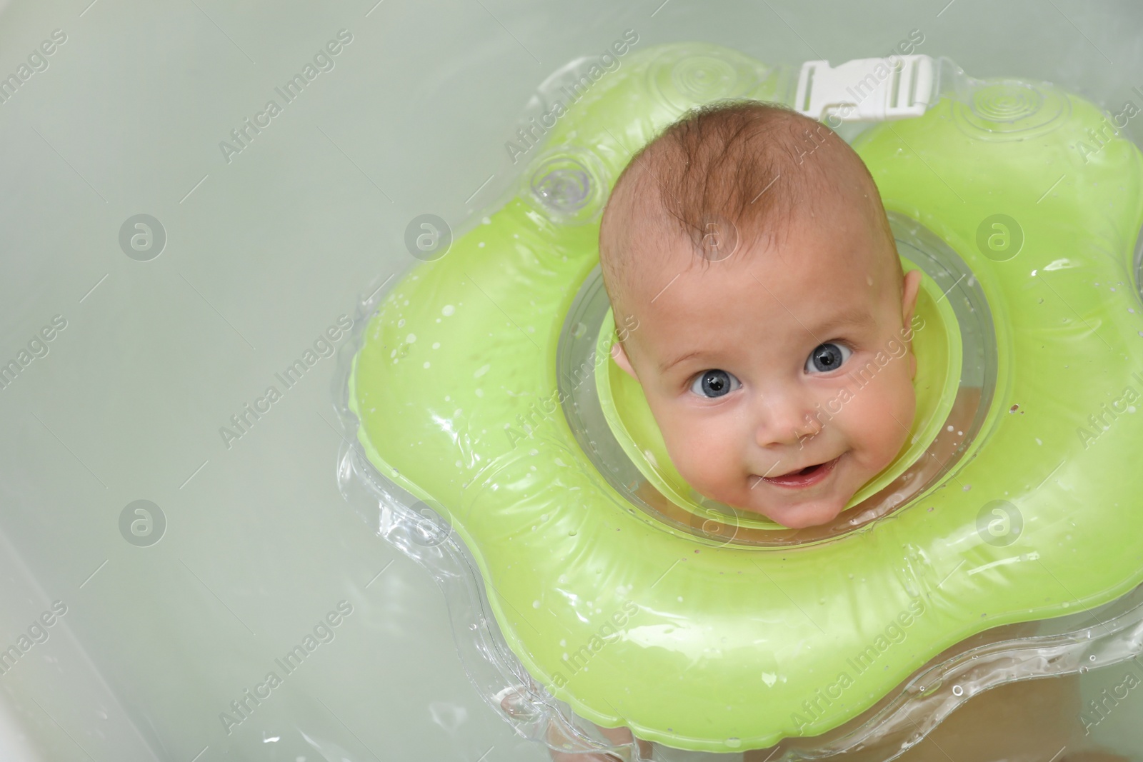 Photo of Cute little baby swimming with inflatable ring in bath, above view