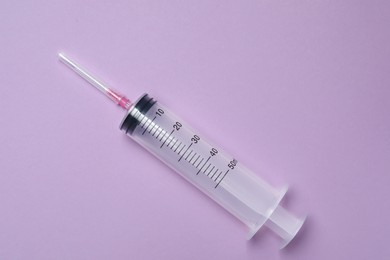 Disposable syringe with needle on violet background, top view
