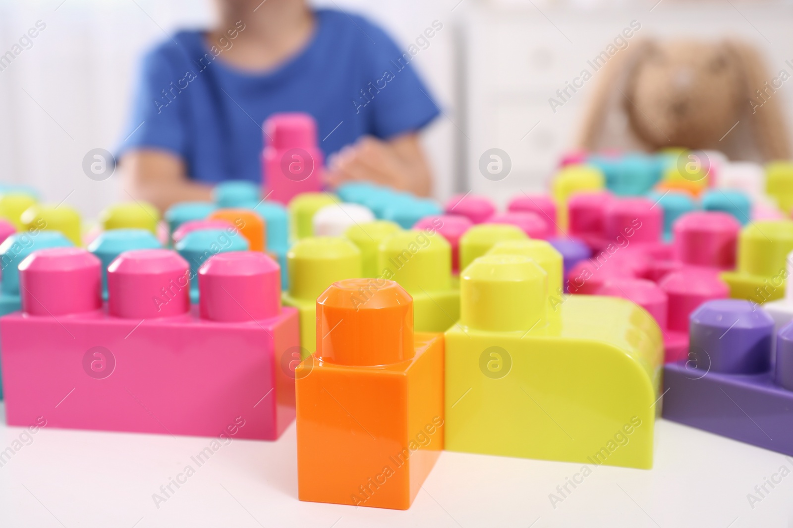 Photo of Little child playing with colorful building blocks at table indoors, closeup