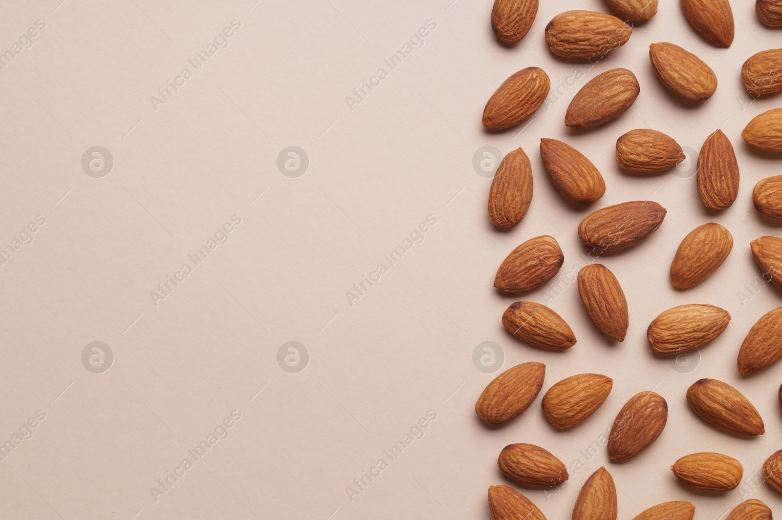 Photo of Delicious raw almonds on beige background, flat lay. Space for text