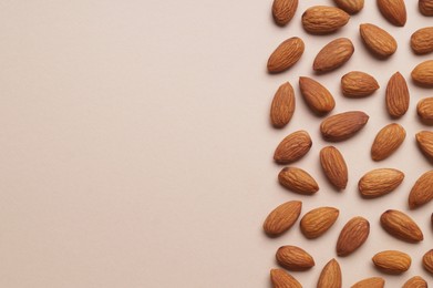 Photo of Delicious raw almonds on beige background, flat lay. Space for text