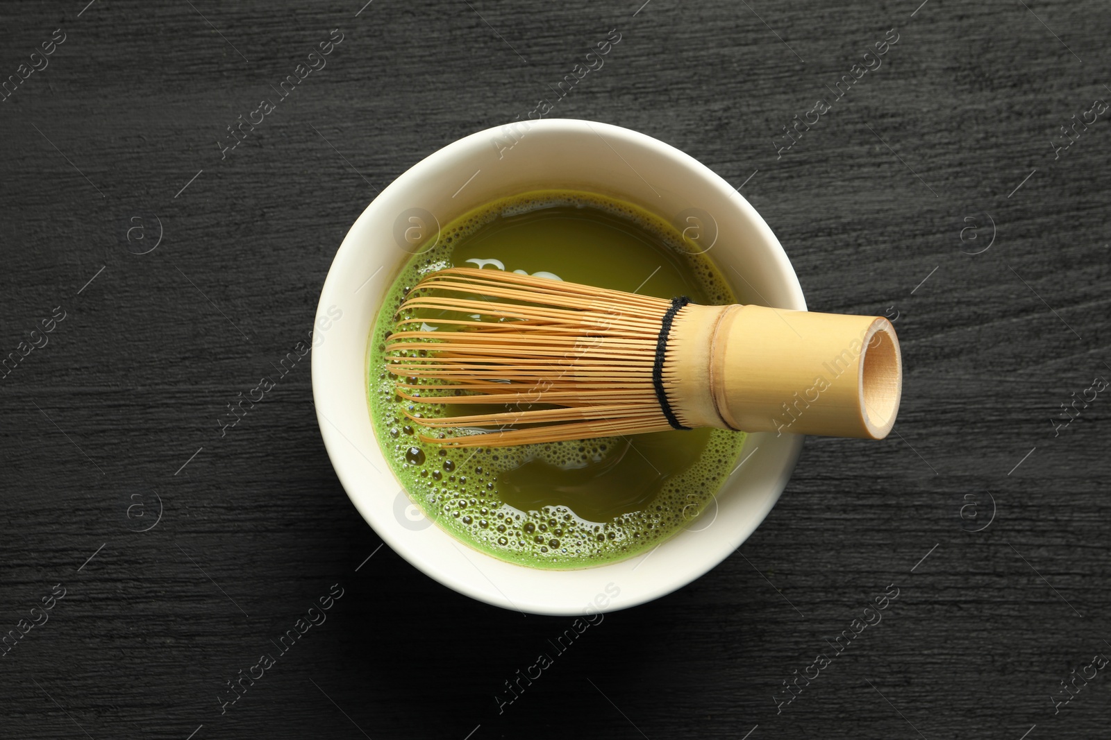 Photo of Cup of fresh matcha tea with bamboo whisk on black wooden table, top view