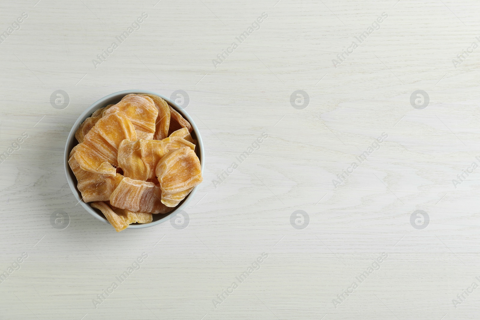 Photo of Delicious dried jackfruit slices in bowl on white wooden table, top view. Space for text