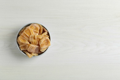 Delicious dried jackfruit slices in bowl on white wooden table, top view. Space for text