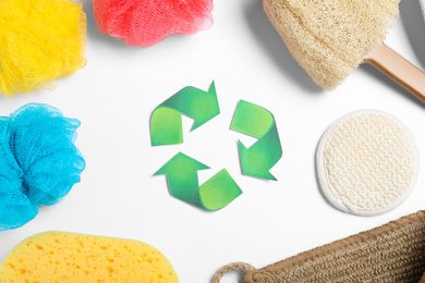 Photo of Recycling symbol, plastic and natural shower sponges on white background, top view