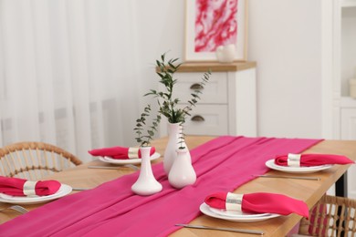 Beautiful table setting and vases with green branches in dining room