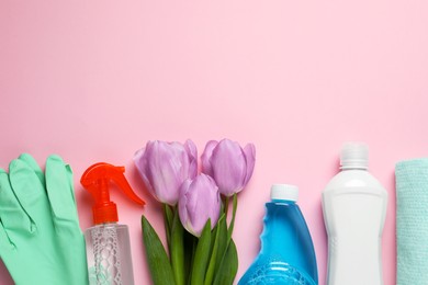 Photo of Spring cleaning. Detergents, flowers, gloves and rag on pink background, flat lay. Space for text