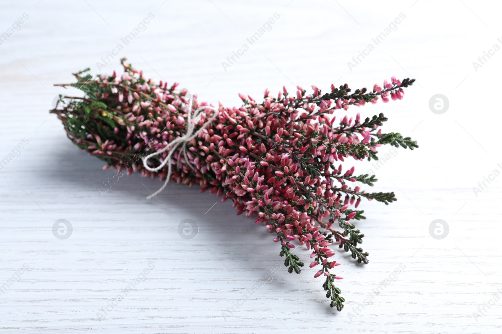 Photo of Bunch of heather branches with beautiful flowers on white wooden table, closeup