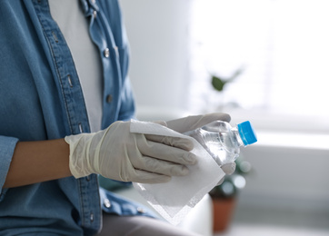 Photo of Woman cleaning bottle of water with wet wipe indoors, closeup