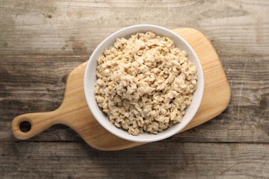 Photo of Tasty boiled oatmeal in bowl on wooden table, top view