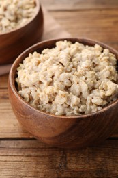 Photo of Tasty boiled oatmeal in bowl on wooden table, closeup