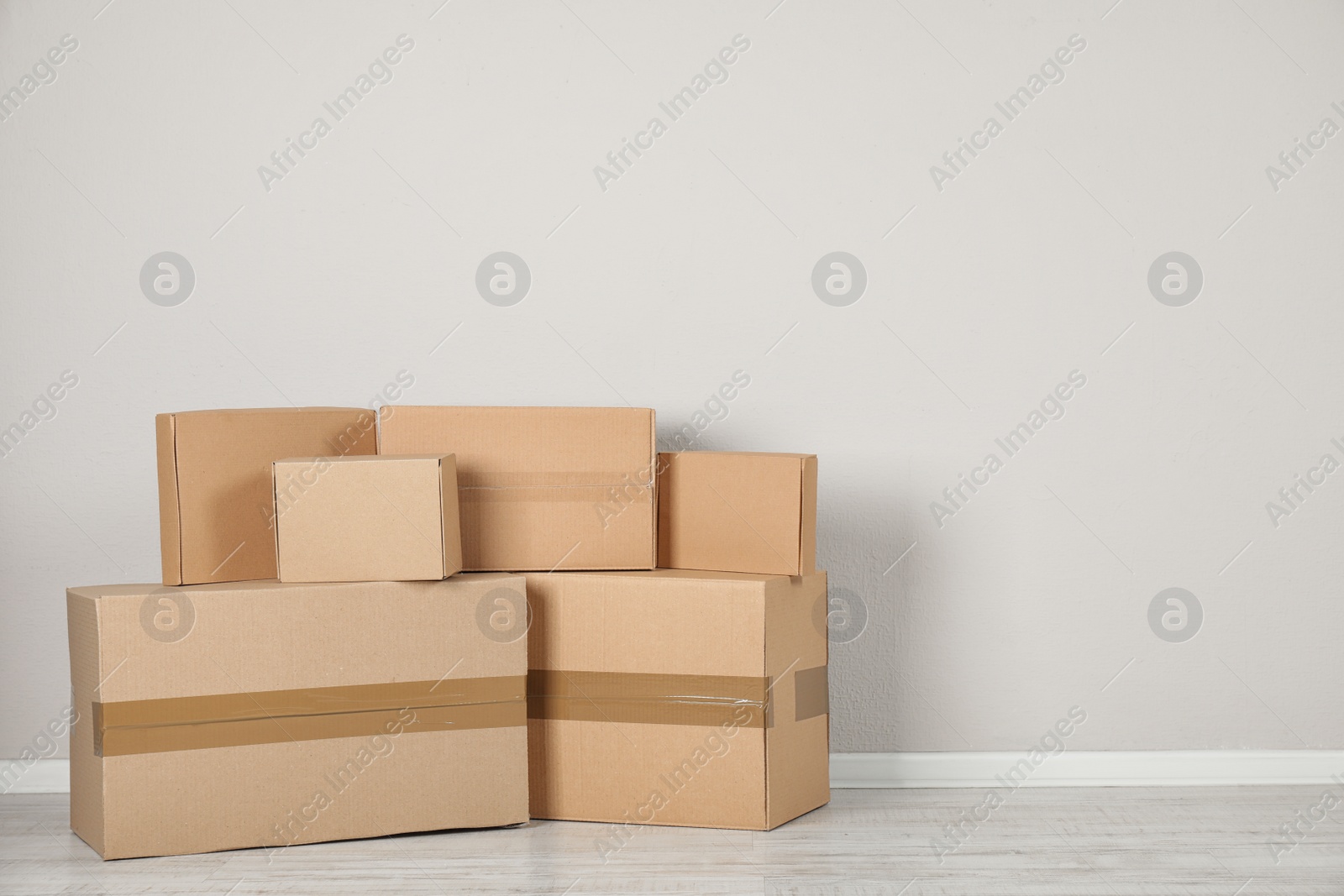 Photo of Pile of cardboard boxes near light wall indoors. Space for text