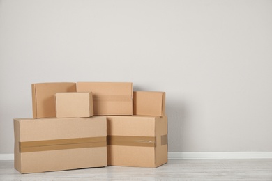 Photo of Pile of cardboard boxes near light wall indoors. Space for text