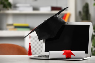 Graduation hat, student's diploma and laptop on white table indoors
