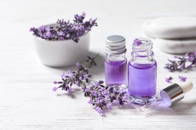 Photo of Glass bottles of natural cosmetic oil and lavender flowers on white wooden table