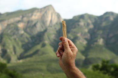 Photo of Man holding palo santo stick in high mountains, closeup