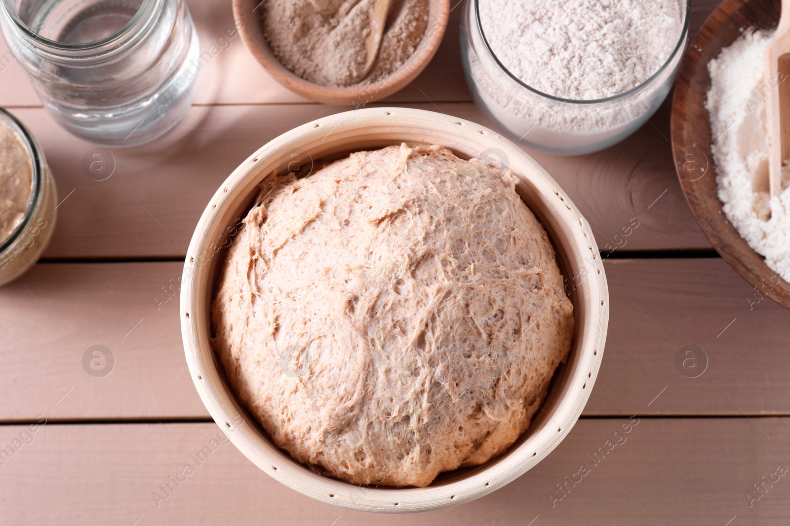 Photo of Fresh sourdough, flour and water on wooden table, flat lay