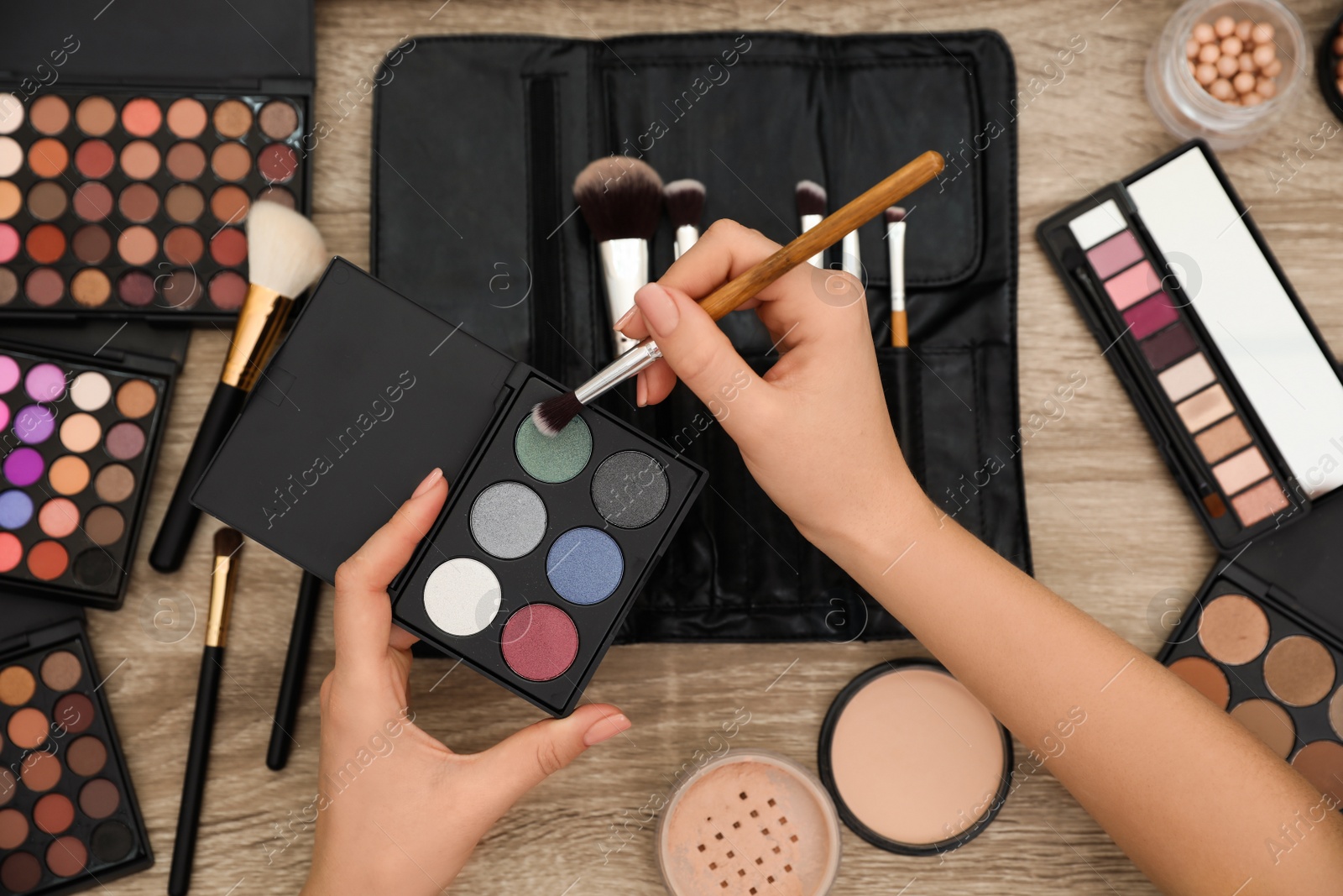 Photo of Professional makeup artist with eyeshadow and brush at wooden table, top view