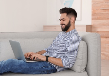 Photo of Handsome young man working with laptop on sofa at home
