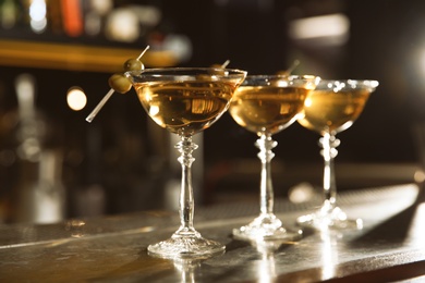 Photo of Glasses of martini cocktail with olives on bar counter. Space for text