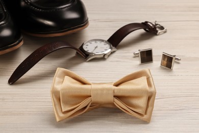 Photo of Stylish beige bow tie, shoes, wristwatch and cufflinks on white wooden background