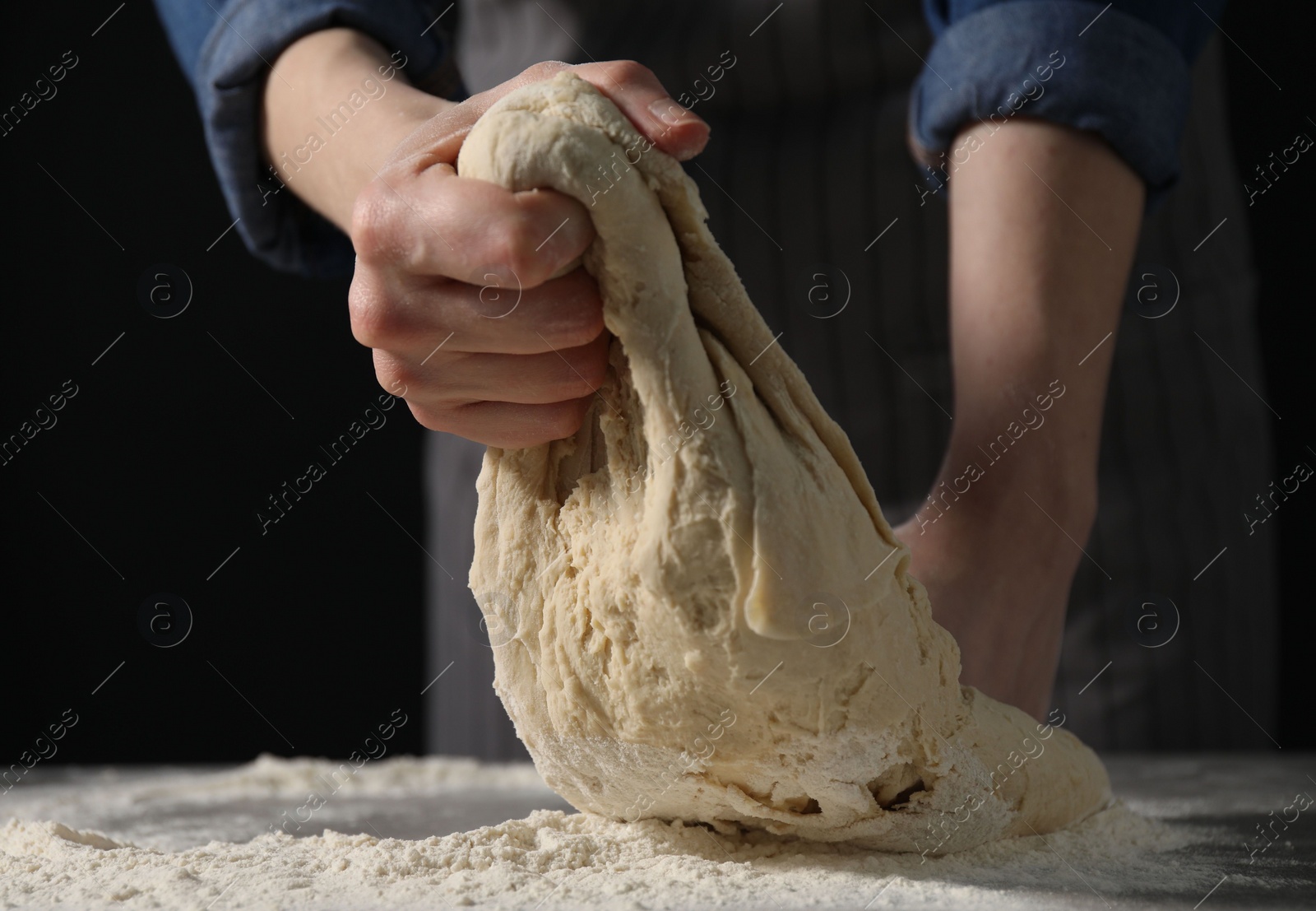 Photo of Making bread. Woman kneading dough at table on dark background, closeup. Space for text