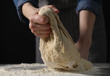 Making bread. Woman kneading dough at table on dark background, closeup. Space for text