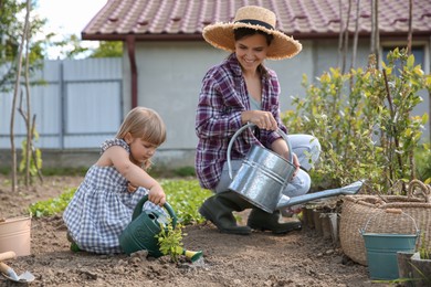 Photo of Mother and her cute daughter planting tree together in garden