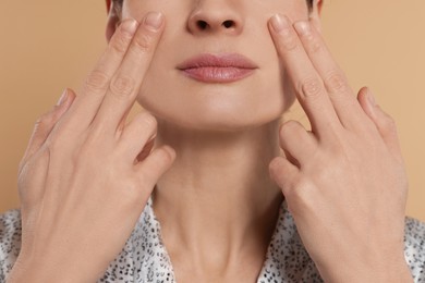 Woman massaging her face on beige background, closeup