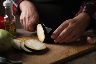 Photo of Cooking delicious ratatouille. Woman cutting fresh eggplant at wooden table, closeup
