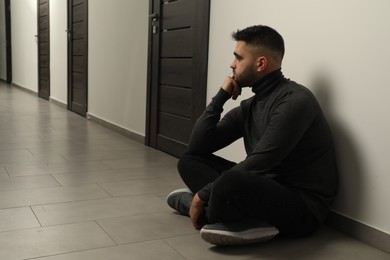 Photo of Sad man sitting on floor in hall. Space for text