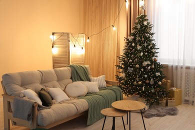 Photo of Comfortable sofa and coffee table near Christmas tree in room