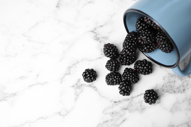 Overturned mug with blackberries on white marble table, flat lay. Space for text