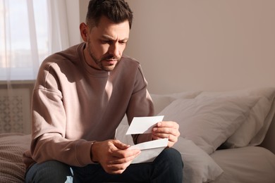 Upset man with envelope in bedroom. Loneliness concept