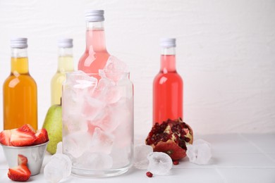 Tasty kombucha in bottles, glass with ice and fresh fruits on white table, space for text