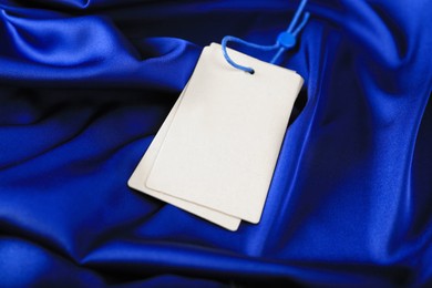 Photo of Blank white tags on blue silky fabric, closeup. Space for text