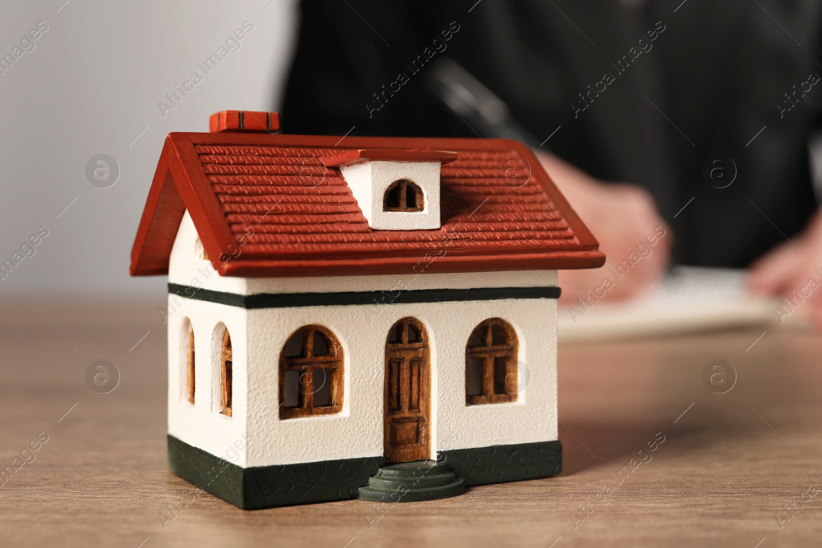 Photo of Mortgage concept. Woman writing at wooden table, focus on house model