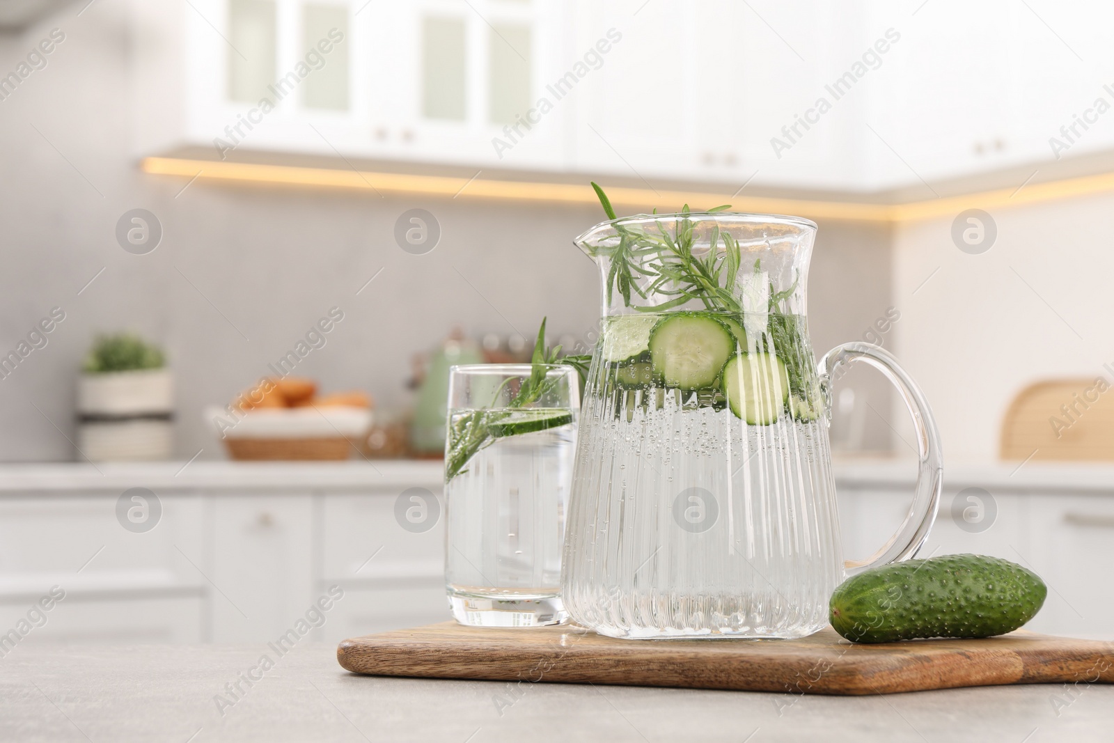 Photo of Refreshing cucumber water with rosemary and vegetable on table in kitchen. Space for text