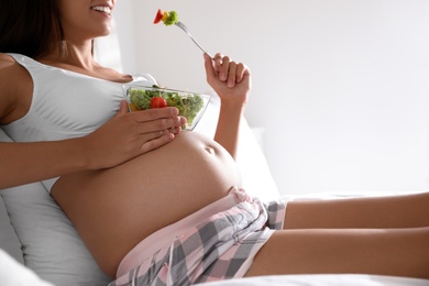 Young pregnant woman with bowl of vegetable salad in bedroom, closeup. Taking care of baby health