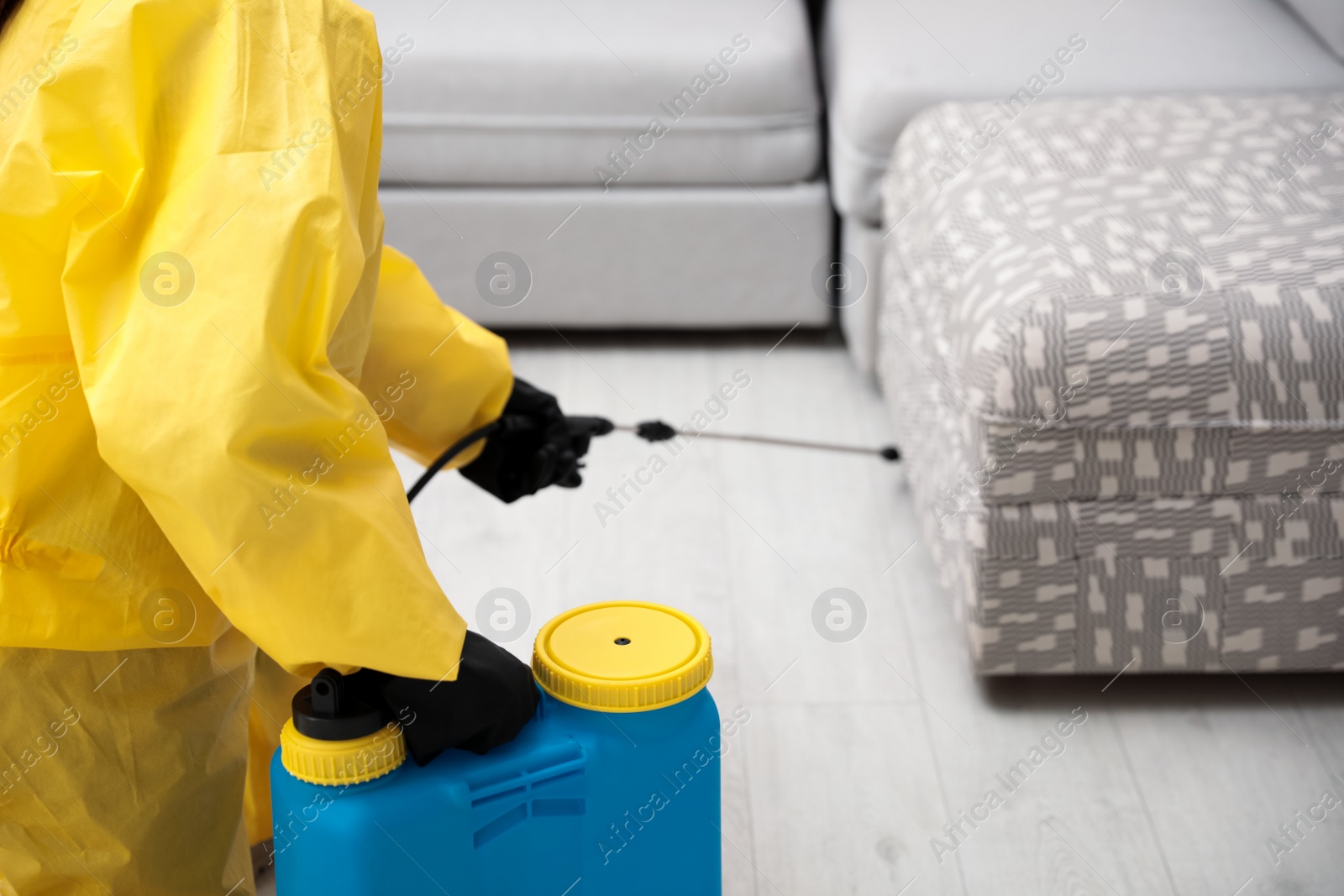 Photo of Pest control worker spraying pesticide under furniture indoors, closeup