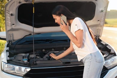 Photo of Stressed young woman talking on phone near broken car on roadside