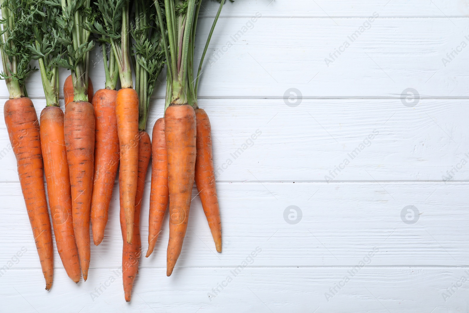 Photo of Ripe carrots on white wooden table, flat lay. Space for text