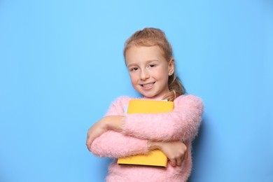 Happy little girl with books on light blue background. Space for text