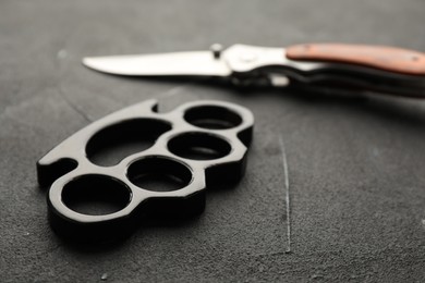 Photo of Brass knuckles and knife on black stone background, closeup