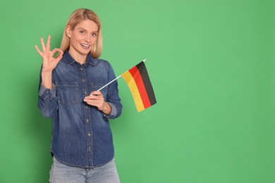 Photo of Woman with flag of Germany showing ok gesture on green background, space for text