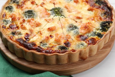 Photo of Pieces of delicious homemade quiche with salmon and broccoli on wooden board, closeup