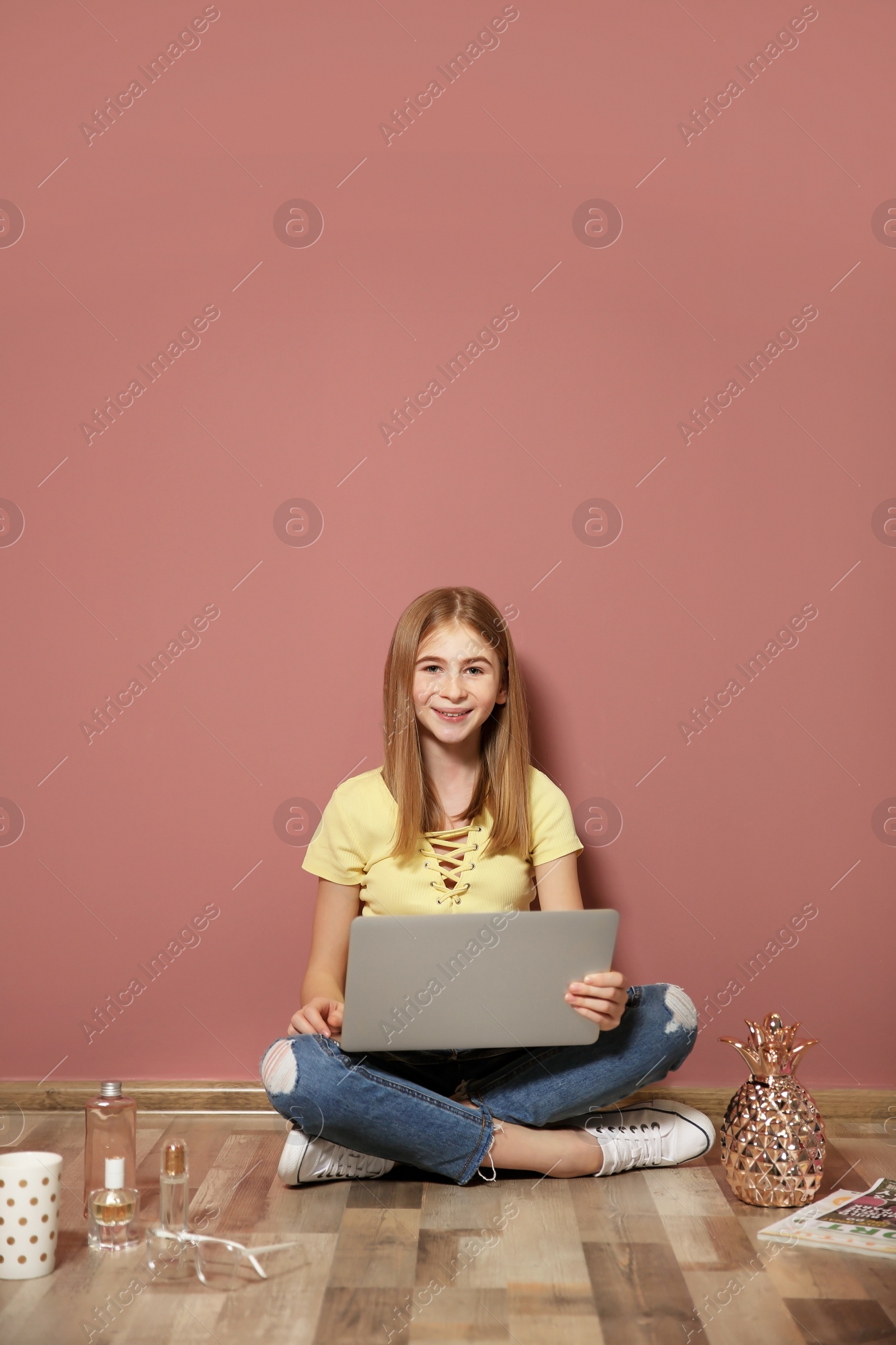 Photo of Cute teenage blogger with laptop sitting on floor against color wall