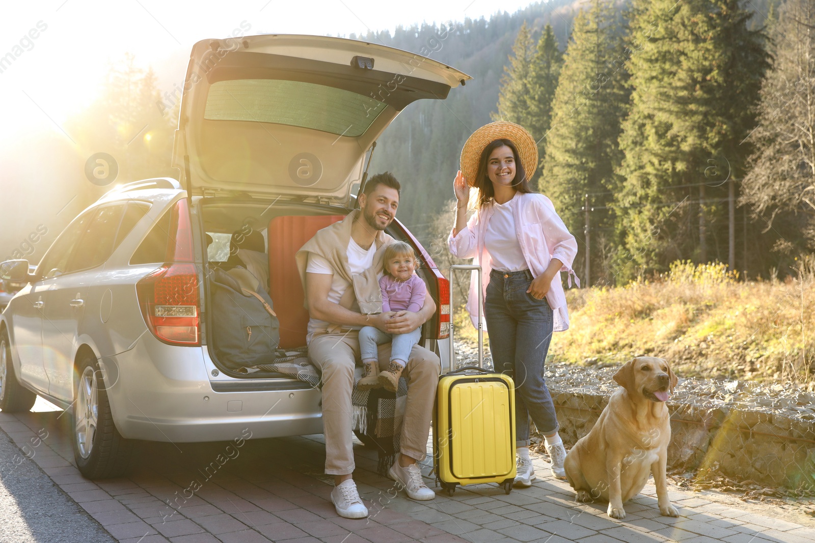 Photo of Parents, their daughter and dog near car outdoors. Family traveling with pet