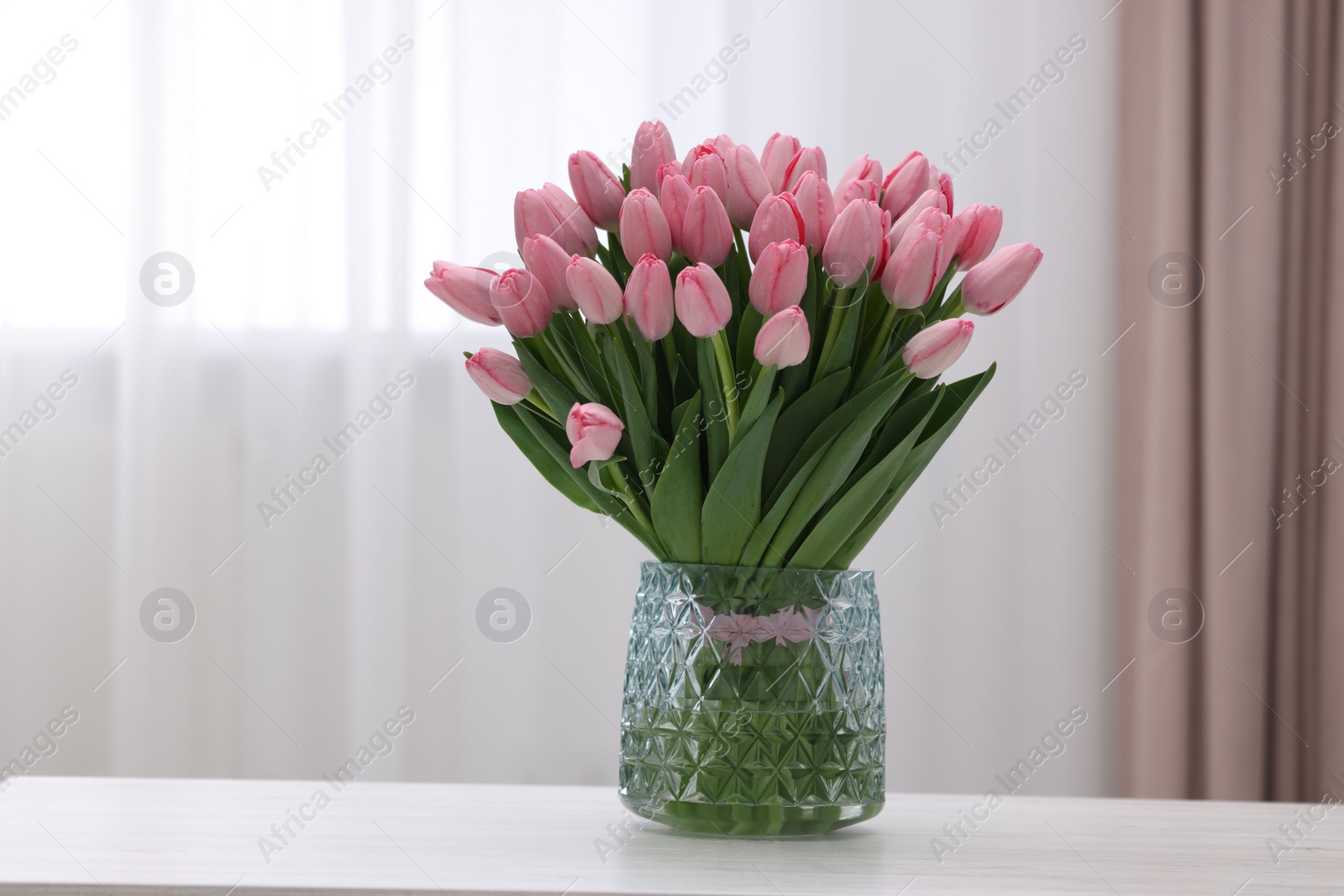 Photo of Bouquet of beautiful pink tulips in vase on white wooden table indoors